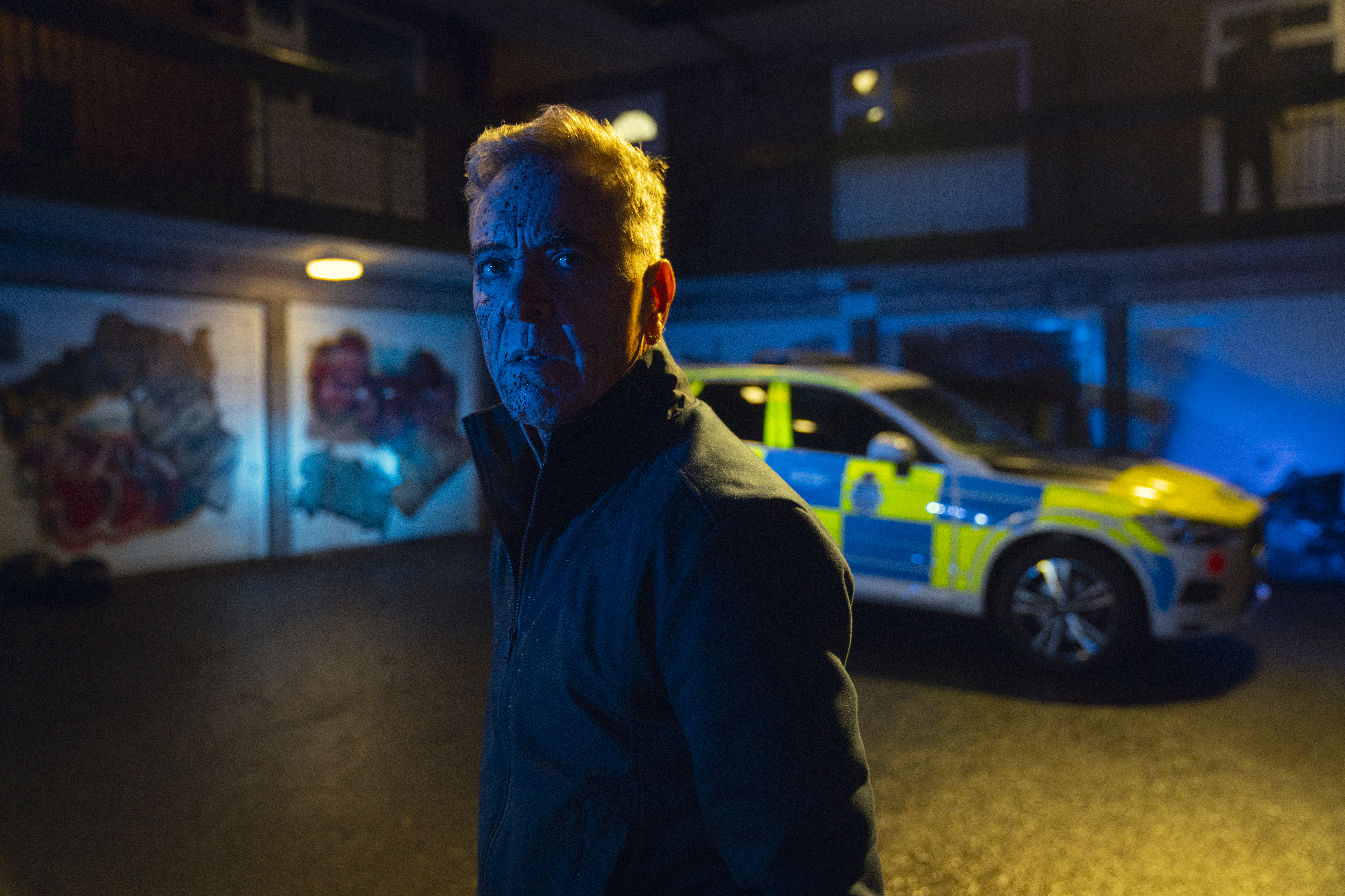 James Nesbitt as Simon in Netflix's Run Away, with blood on his face and a police car in the background.